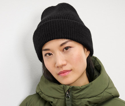 Nő fekete kötött sapkát és zöld kabátot visel.