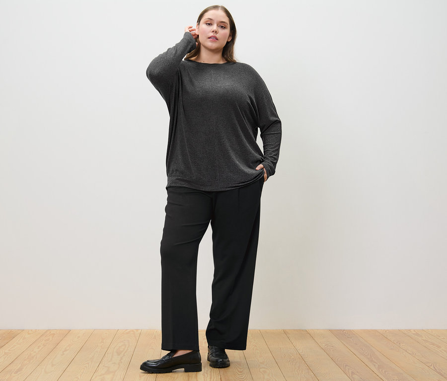 Nő pózol fekete női jersey nadrágban és melírozott sötétszürke női denevérujjú felsőben.