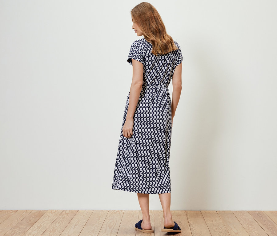 Nő áll háttal a kamerának, mintás jersey midiruhát visel.