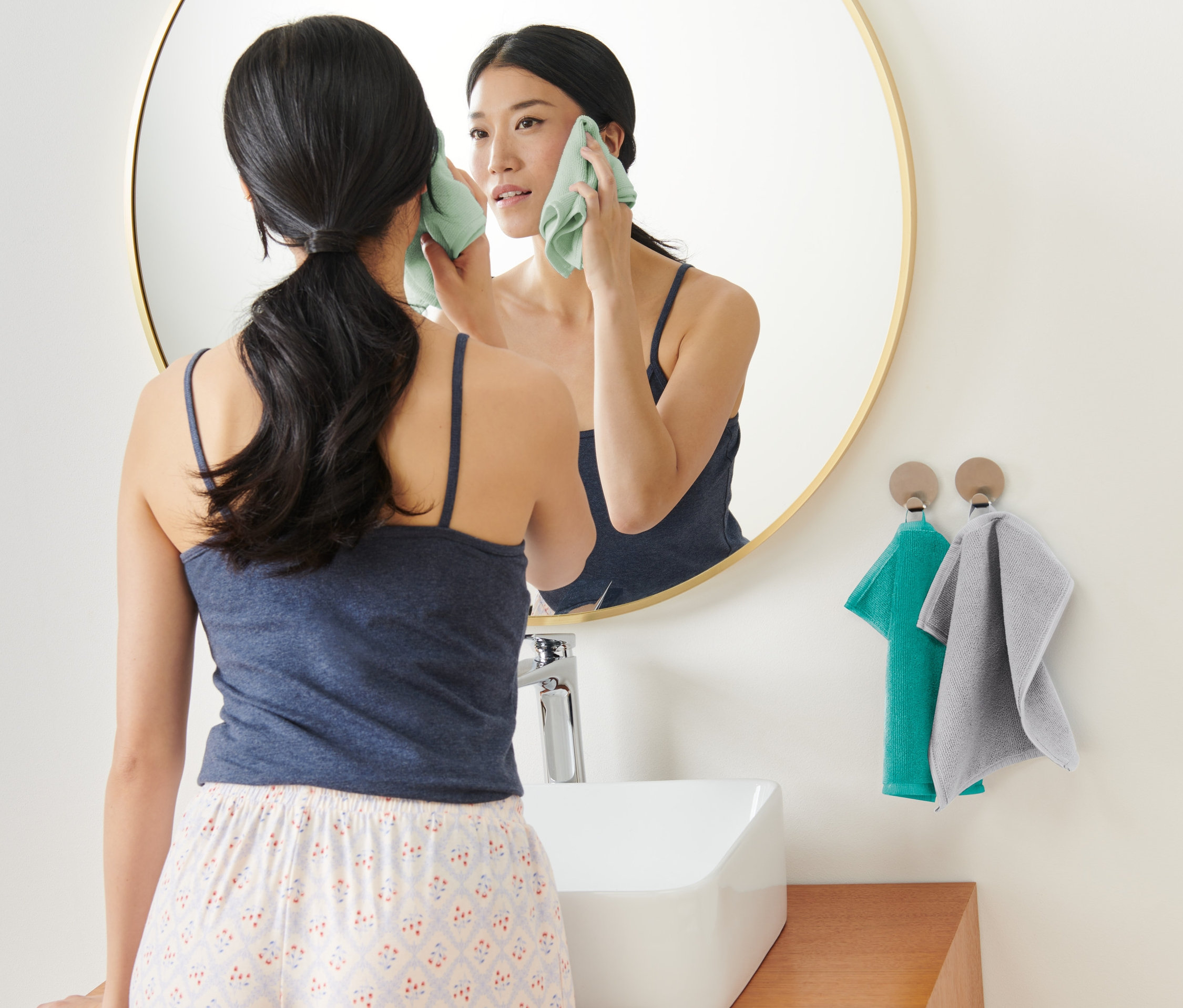 Egy nő az arcát tisztítja egy 3 darabos mikroszálas kozmetikai kendővel a tükör előtt.
