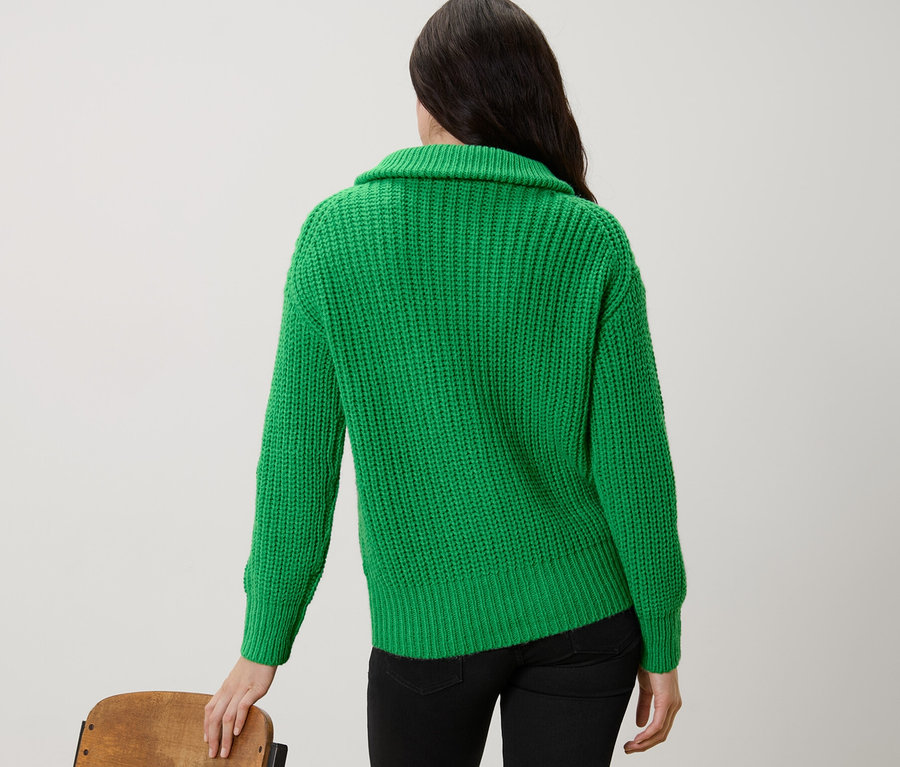 Hátulról látható nő, aki zöld, gyapjúval ellátott, állónyakú pulóvert visel.