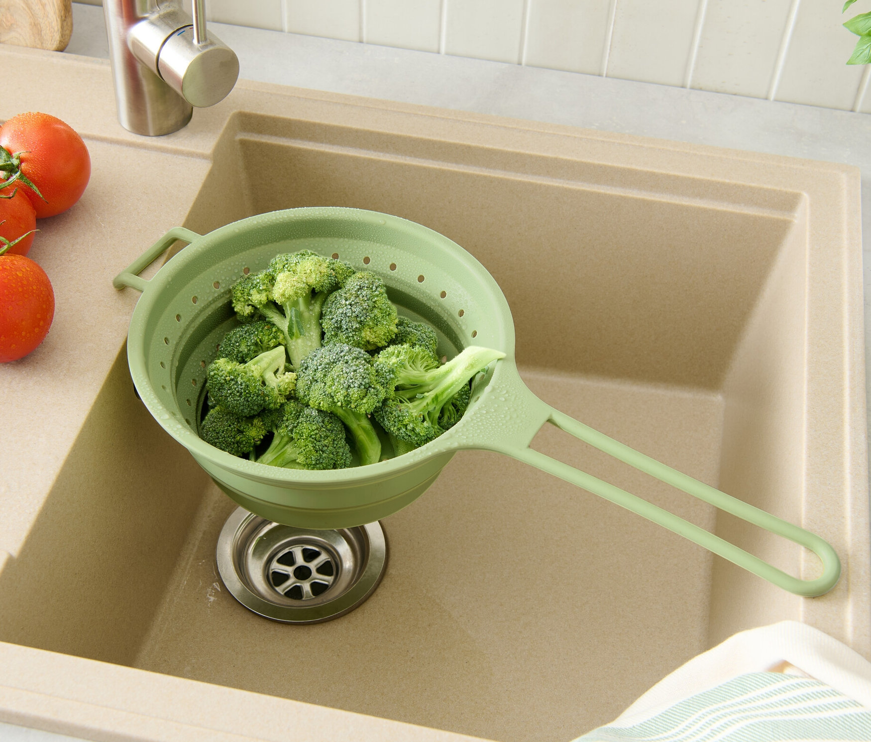 Brokkoli egy zöld helytakarékos szűrőben, egy bézs mosogatóban paradicsommal és fűszernövényekkel.
