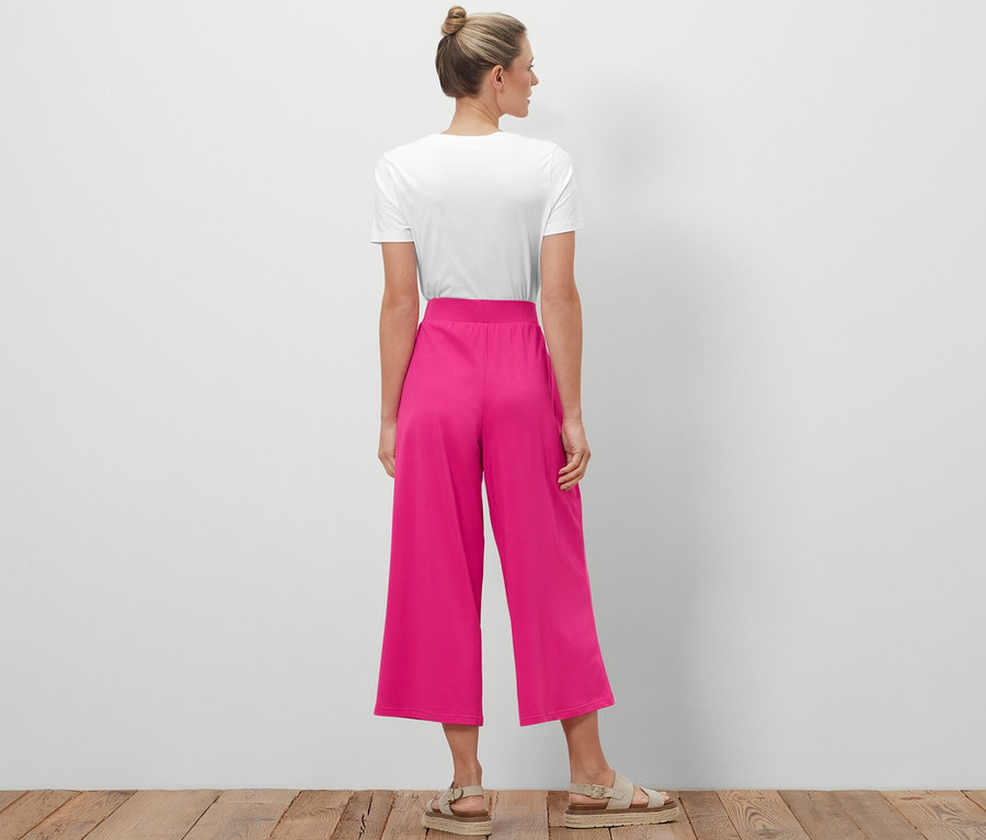 Egy kontyos nő áll háttal a kamerának, bő szárú jerseynadrágot visel.