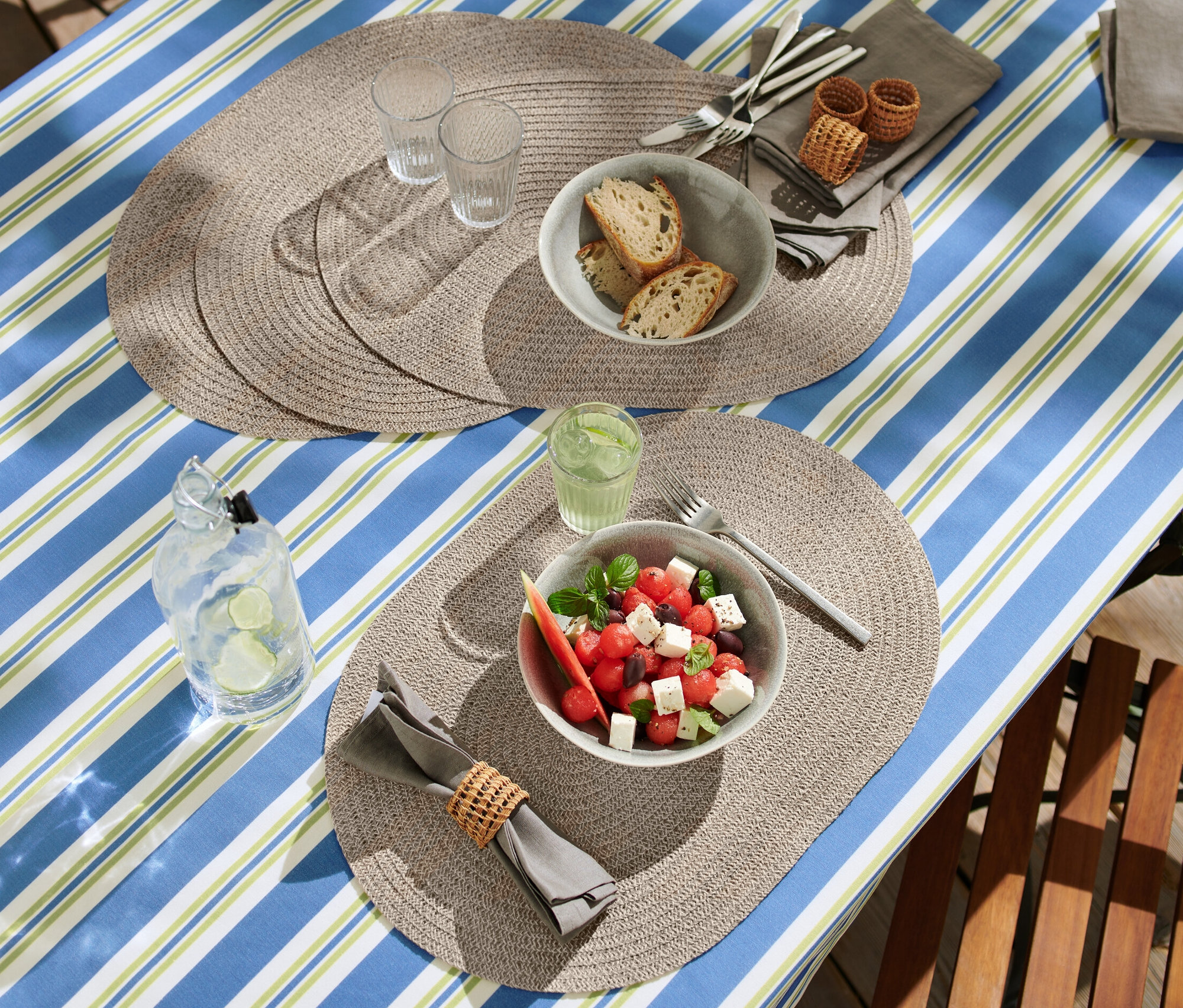 Terített asztal ovális letörölhető tányéralátétekkel, salátával, kenyérrel és italokkal.