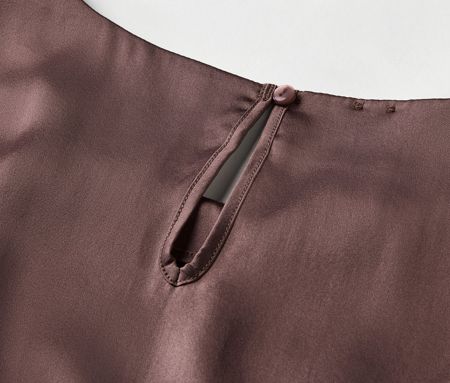 Egy barna szatén felső részlete kulcslyuk kivágással és gombos zárással a nyak hátsó részén.