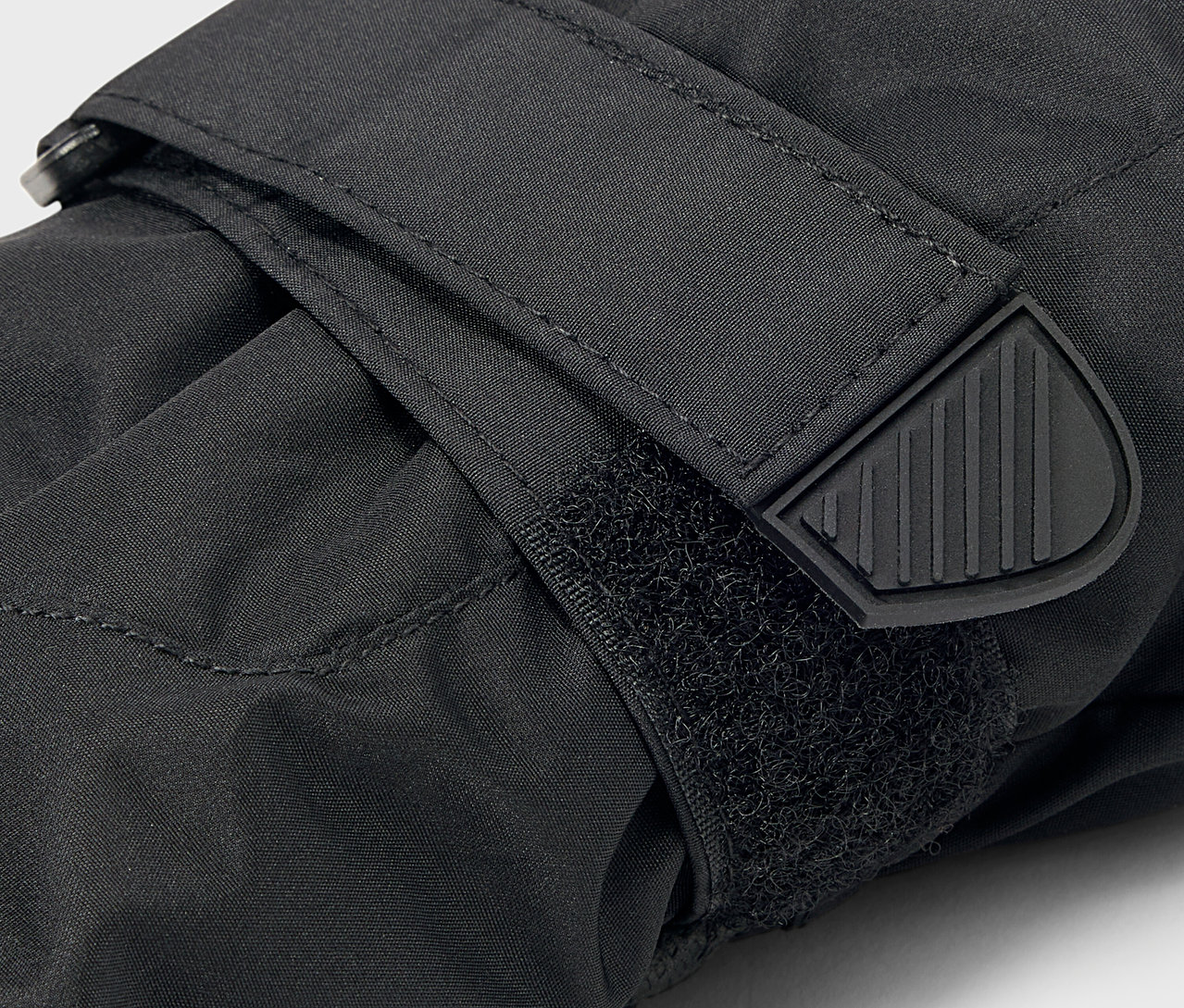 Egy fekete kesztyű részlete tépőzárral és gumi pántvéggel.