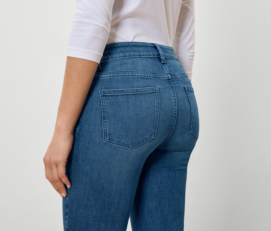 Hátulról látható egy nő kék farmerben és fehér pólóban.