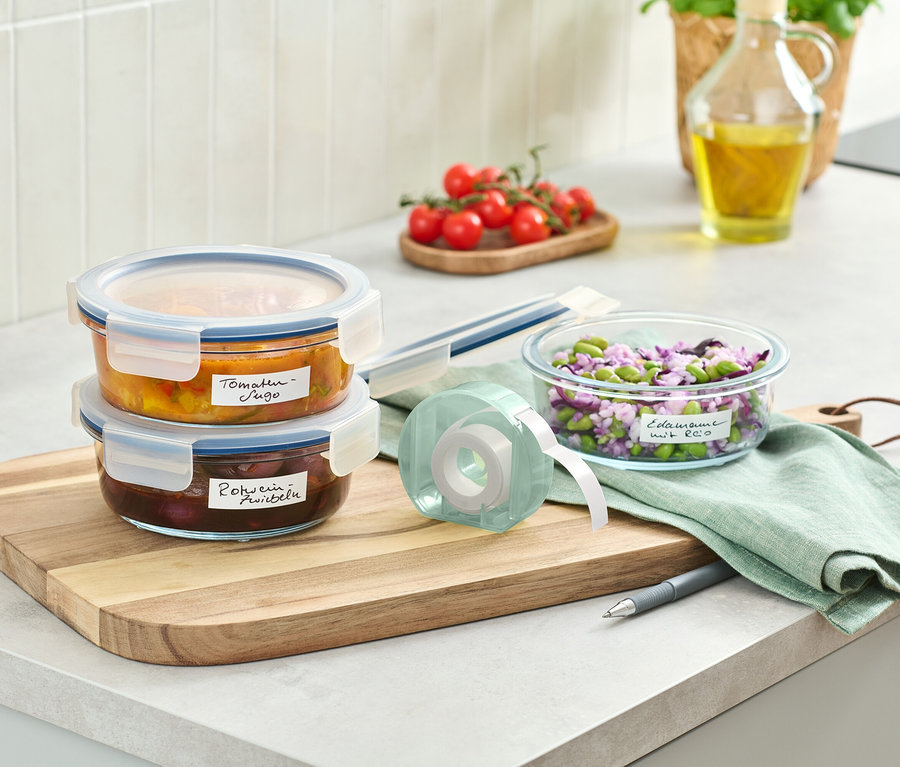 Két üvegtároló edény egymásra rakva egy fa deszkán egy címketekercs mellett.