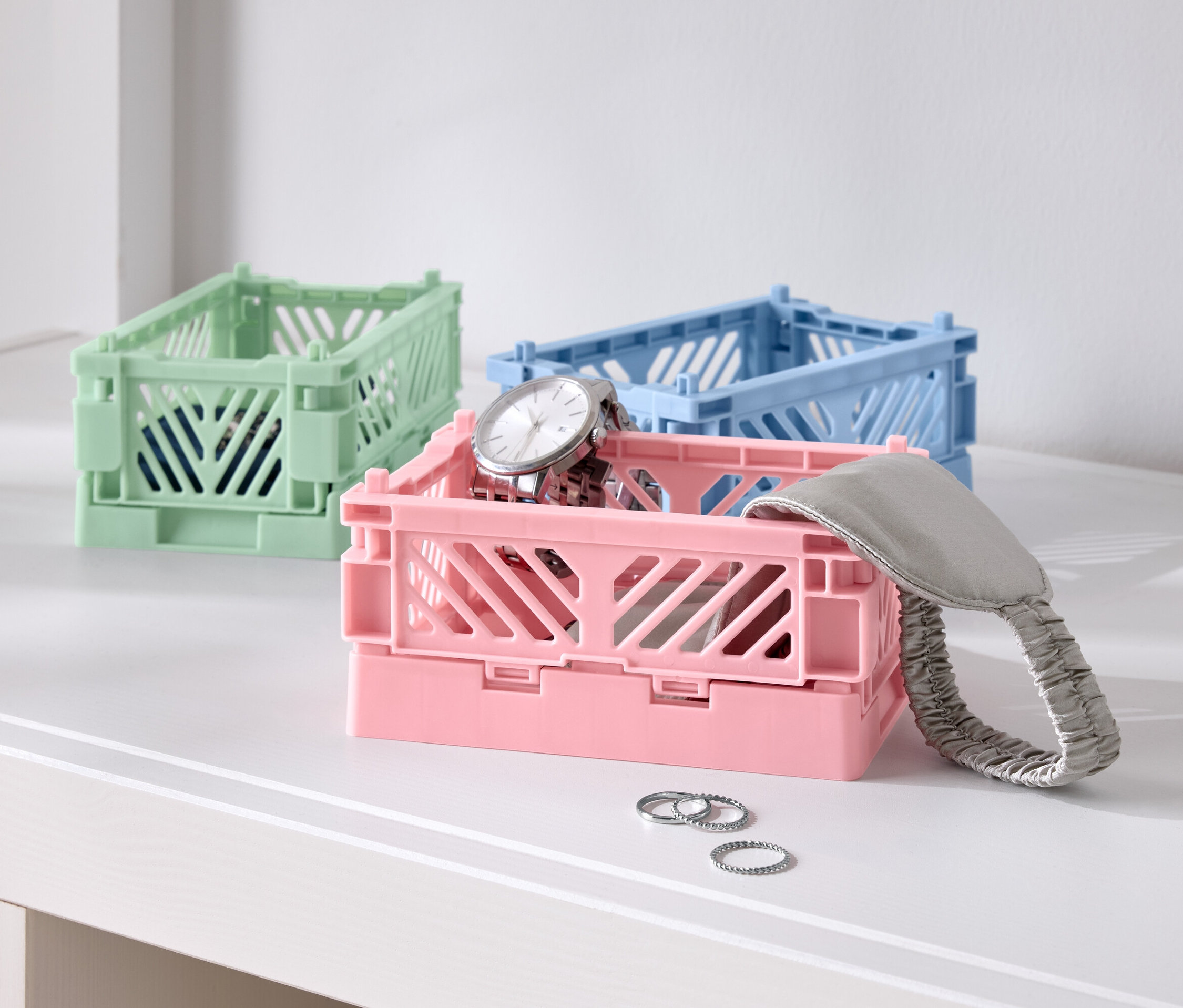 Három színes összecsukható doboz az asztalon, egy rózsaszín órával, egy kék és egy zöld.