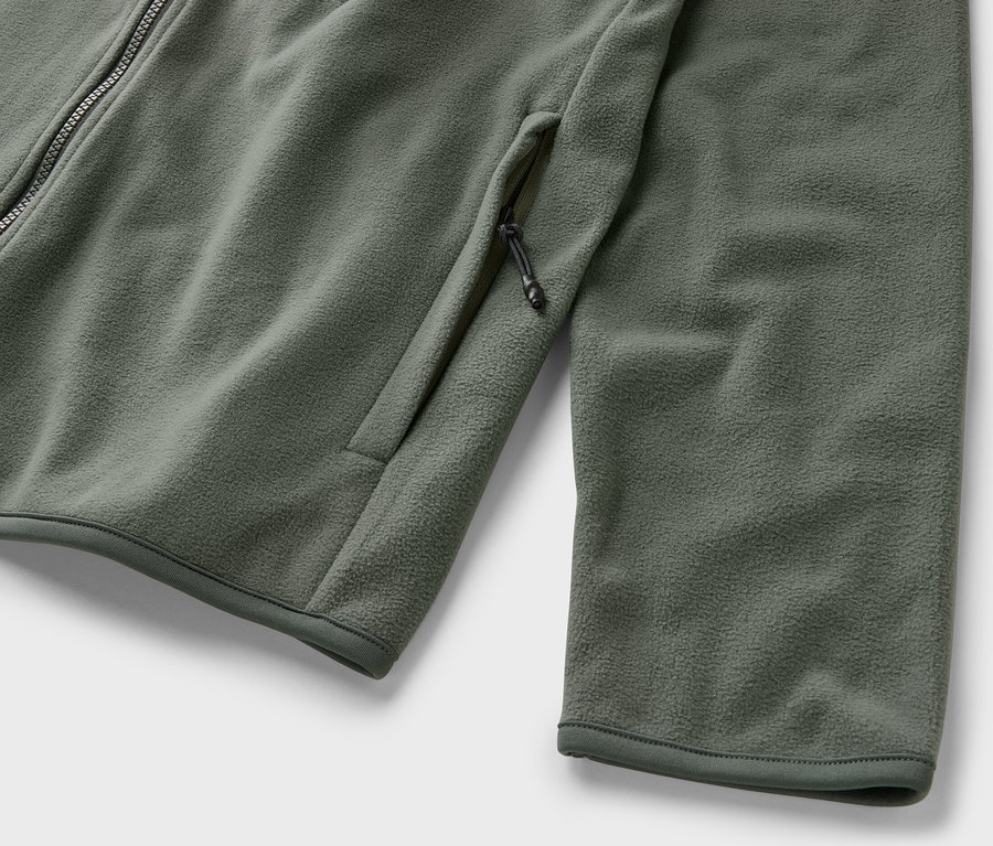 Egy khaki színű, cipzáras, zsebes polár felső részletfotója.