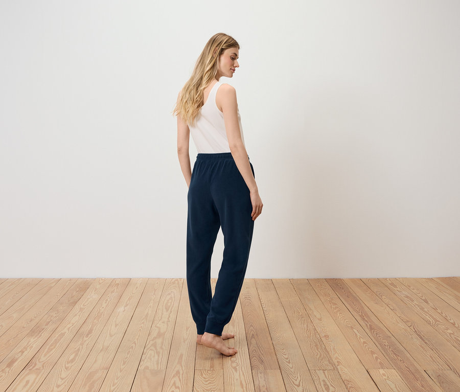 Egy nő áll háttal a kamerának, fehér trikót és sötétkék melegítőnadrágot visel.