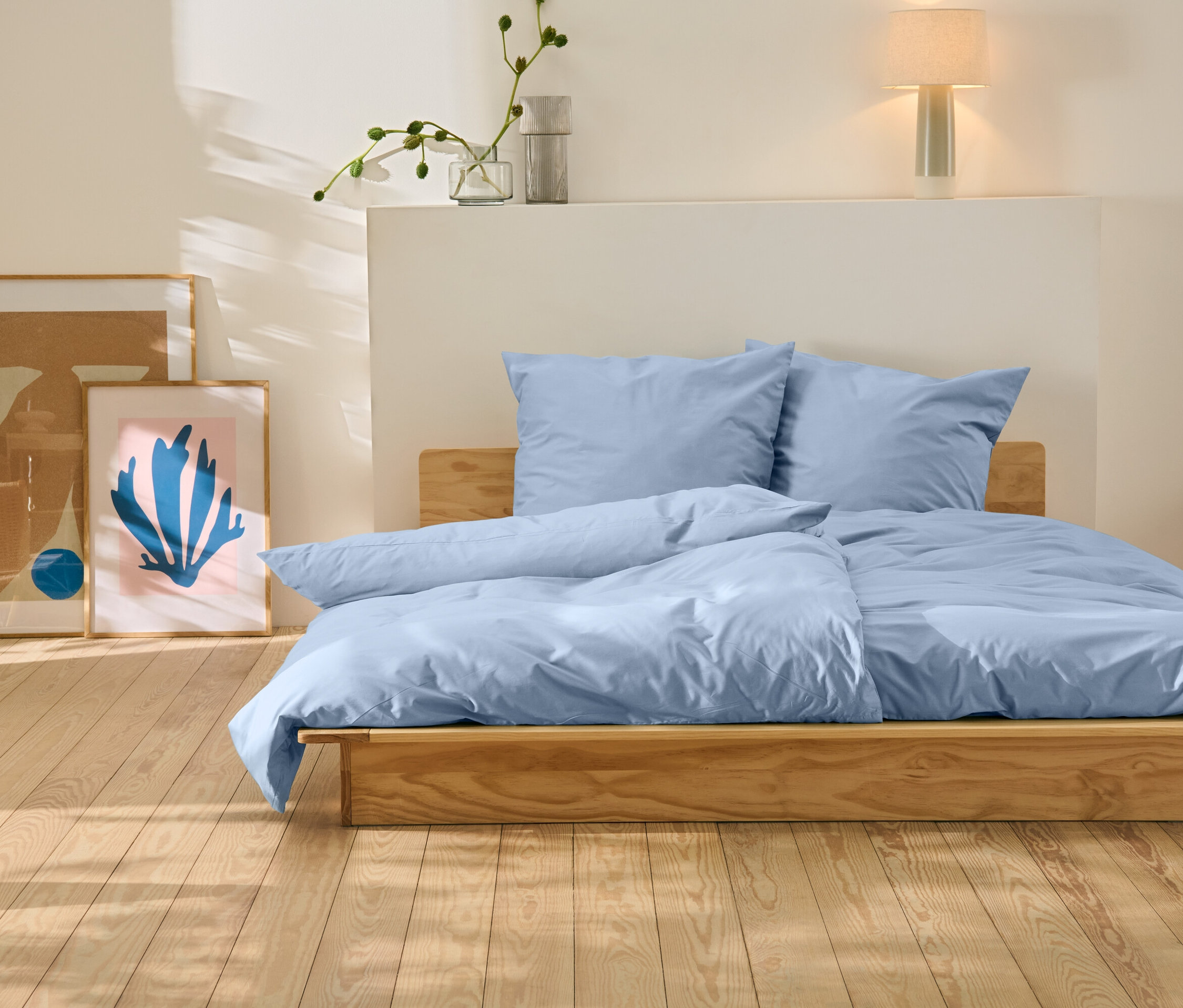 Egy ágy kék ágyneművel áll egy fa padlón. Az ágy mögött két kép található.