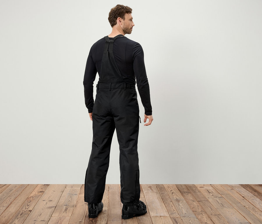 Egy férfi hátulról fekete síkabátot és fekete sícipőt visel.