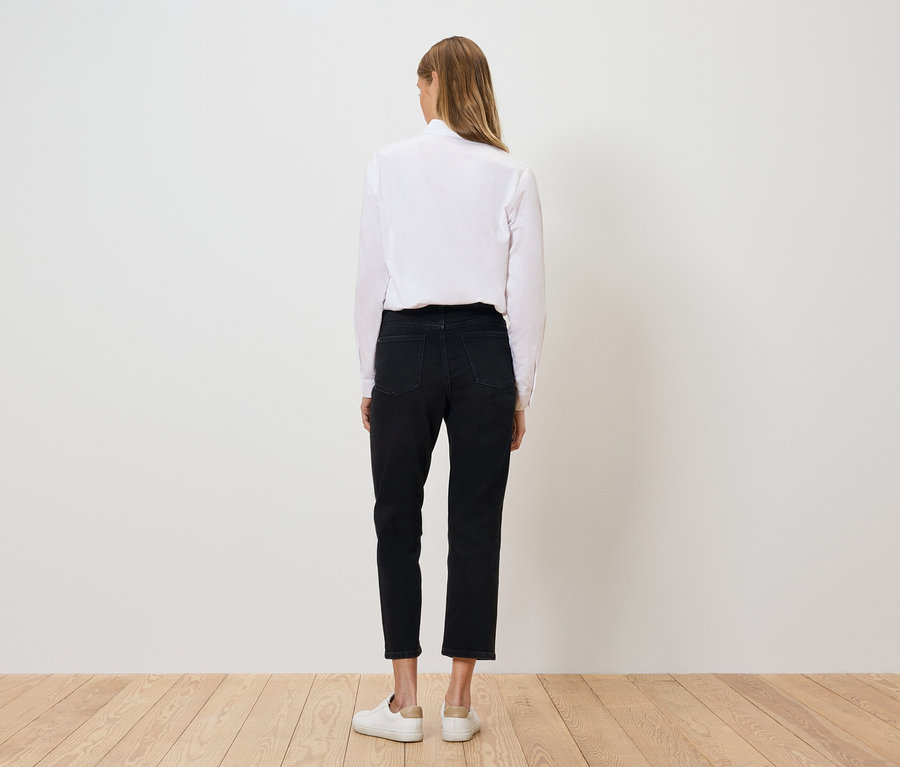 Hátulról látható egy nő fehér ingben, fekete nadrágban és fehér cipőben.