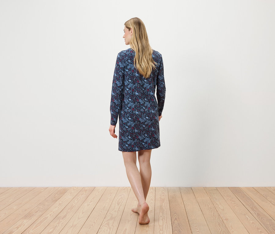 Egy nő háttal a kamerának sétál a fapadlón, kék, hosszú ujjú virágos ruhát visel.