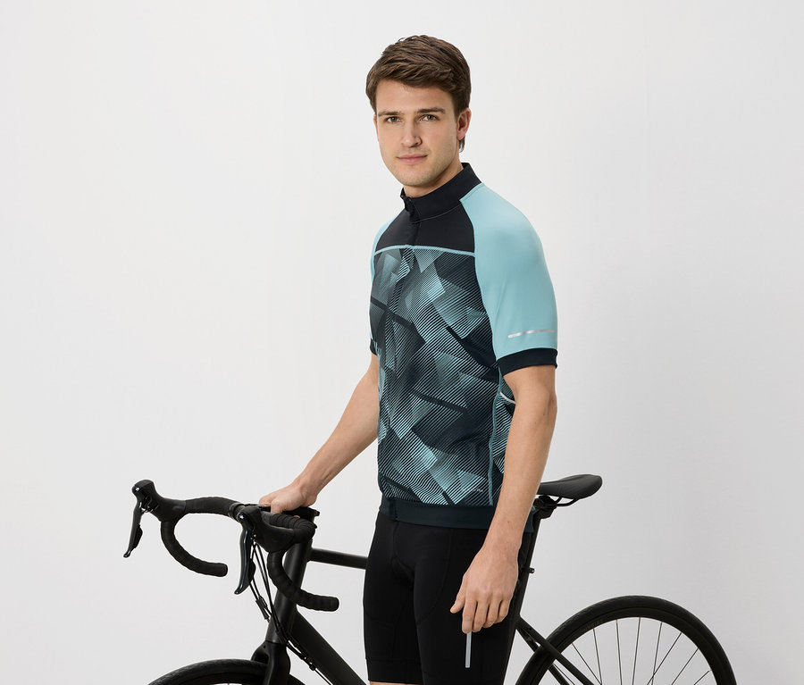 Férfi kerékpáros mezben, kékeszöld ujjal, fekete kerékpárt tart.