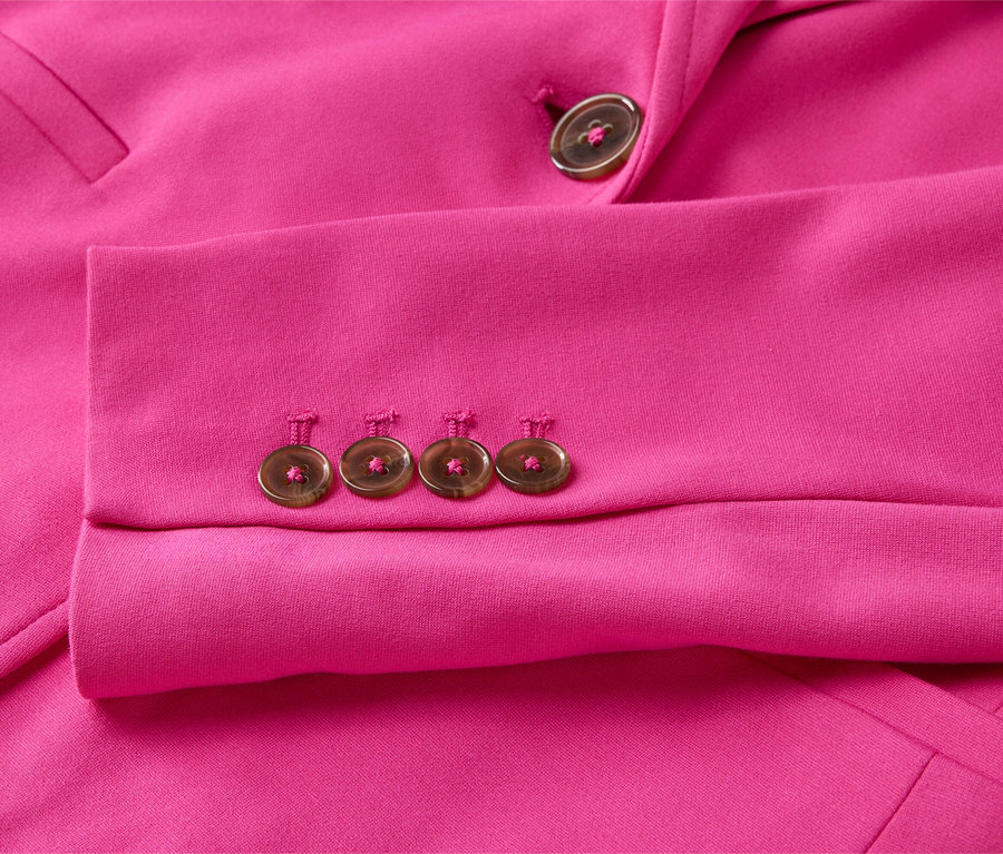 Egy rózsaszín blézer ujjának közeli képe, négy gombbal az ujján és egy gombbal a hajtókán.