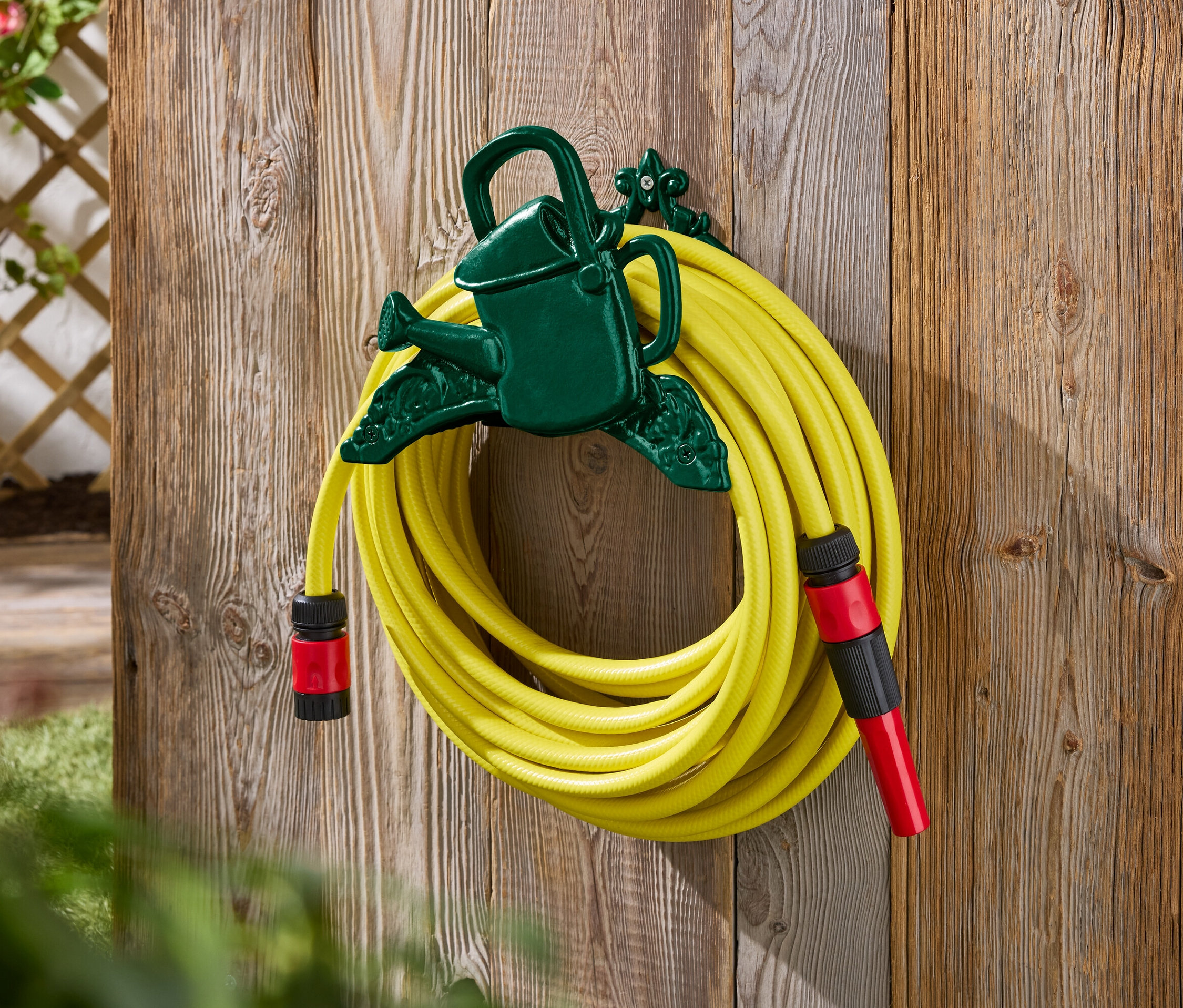 Egy sárga kerti tömlő egy zöld, locsolókanna alakú tartóval van rögzítve egy falfelületre.