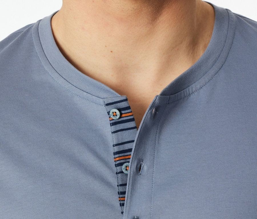Egy férfi közeli képe kék pólóban, gombokkal és csíkos részletekkel.