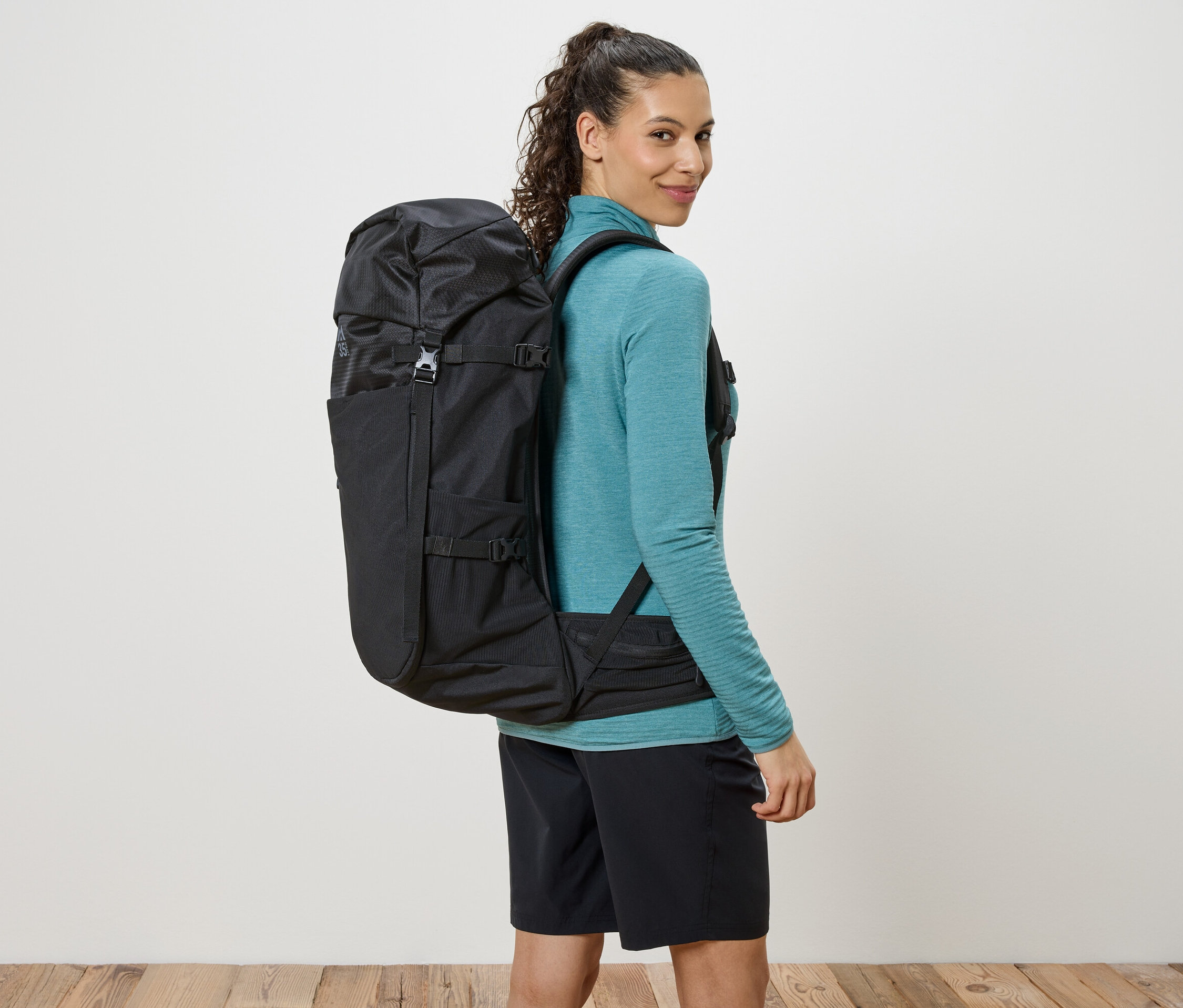 Nő a vállán átvetett fekete hátizsákkal, a válla fölött néz.