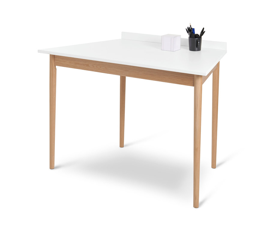 Fehér, trapéz alakú íróasztal négy fa lábbal és egy fekete bögrével, benne írószerekkel.