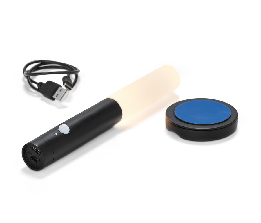 Egy fekete, akkus, multifunkciós LED-lámpa, egy töltőkábel és egy talp fehér háttér előtt.