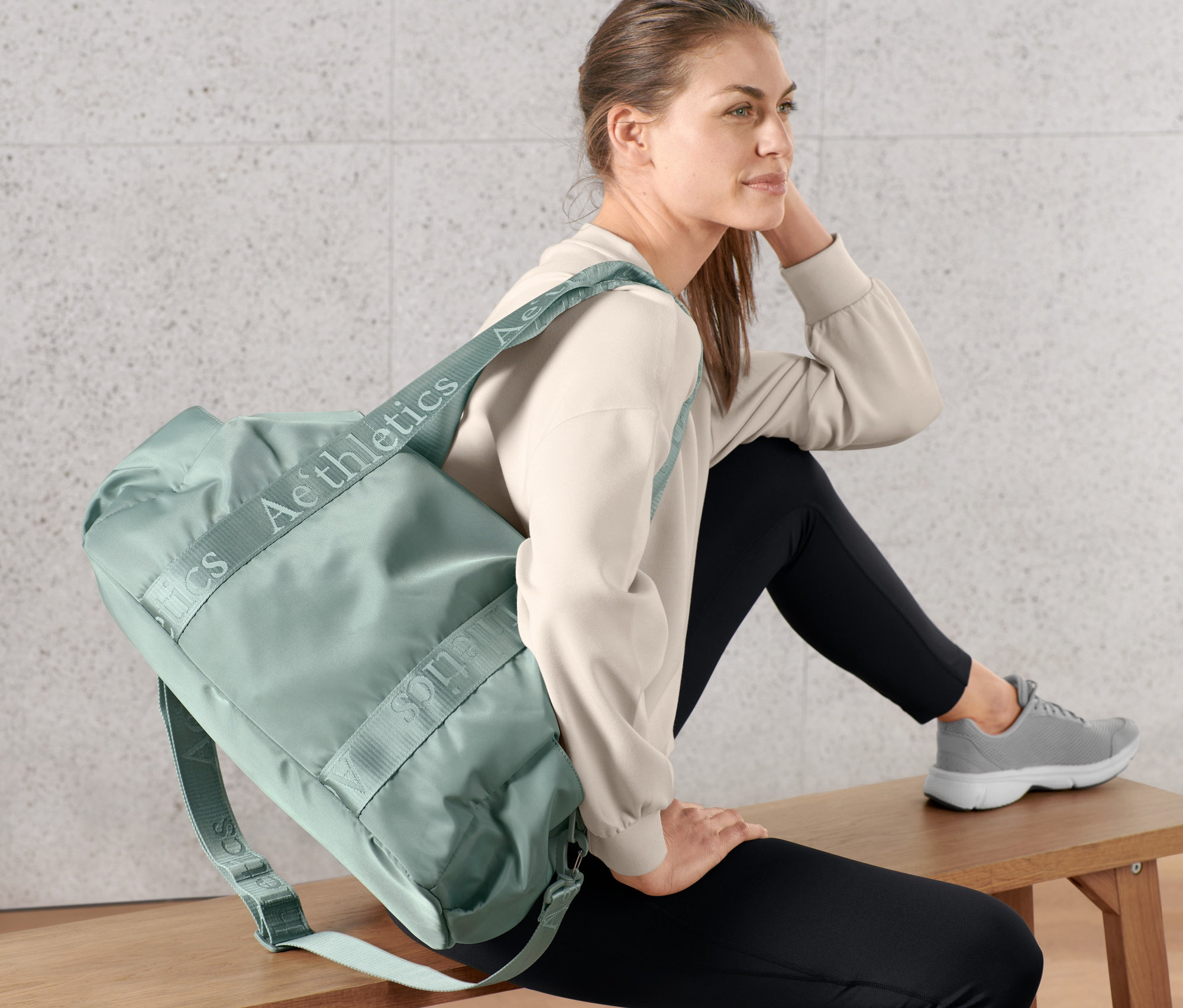 Egy nő ül egy padon, és egy sporttáska van a vállán.