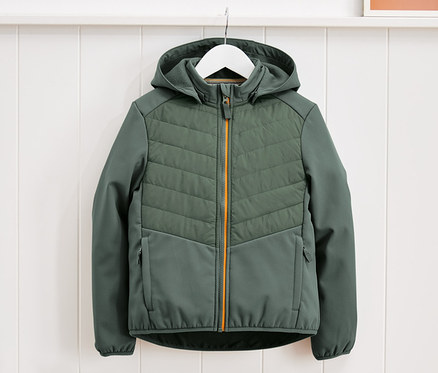 Egy zöld hibrid dzseki lóg egy fehér akasztón egy fehér fal előtt.