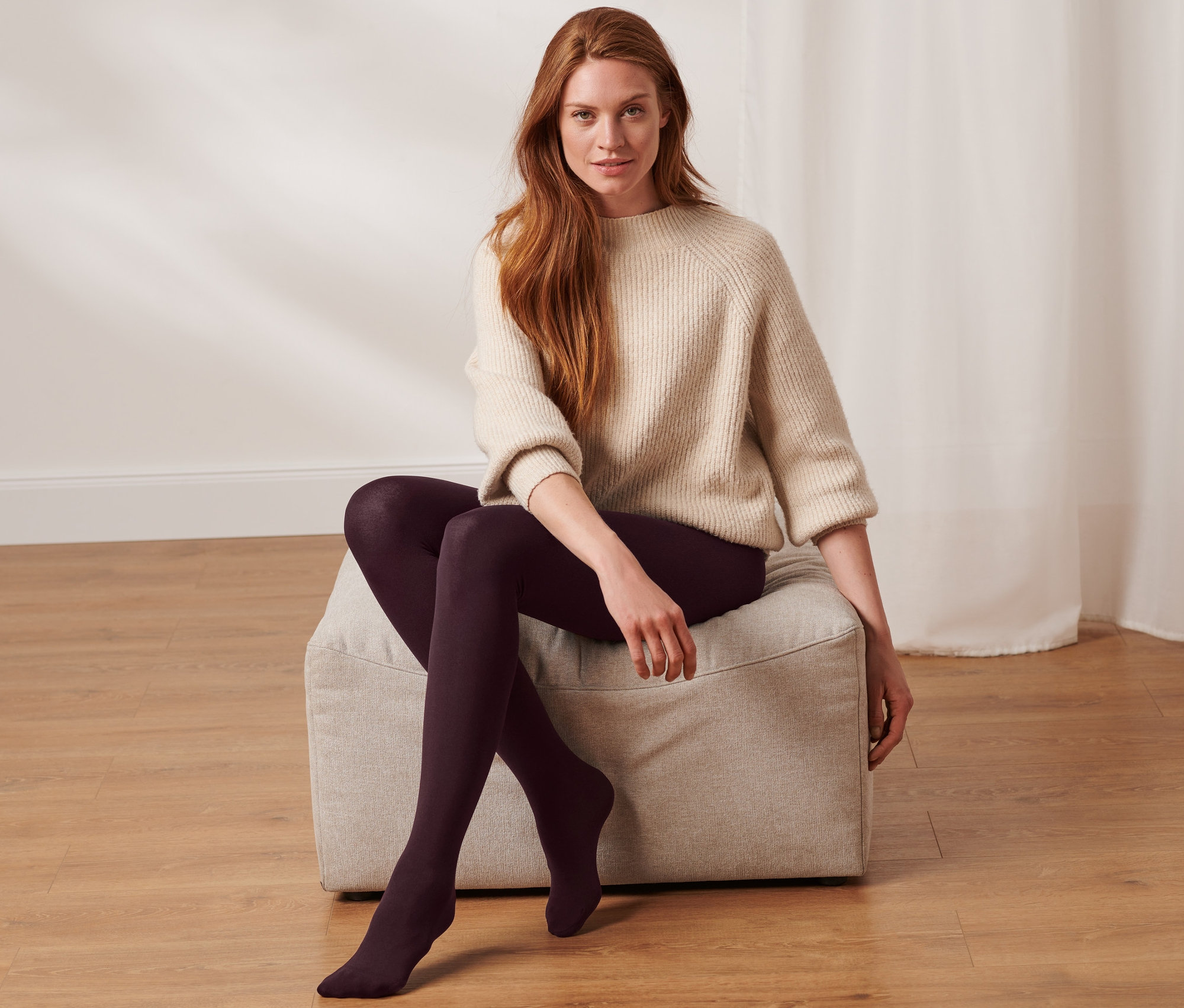Nő ül egy puffon, és női termo harisnyanadrágot visel.
