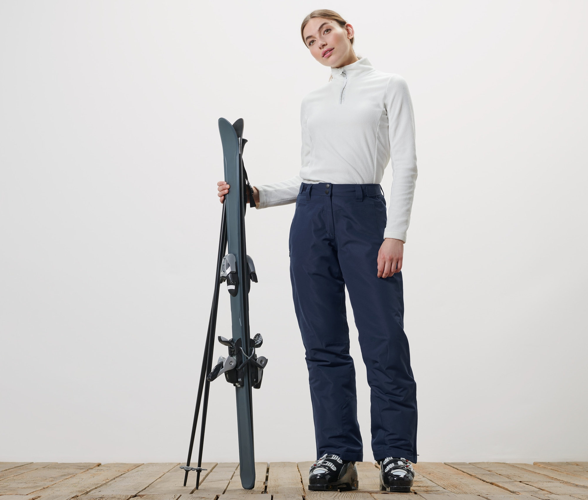 Nő tartja a síket és sötétkék női sínadrágot visel.