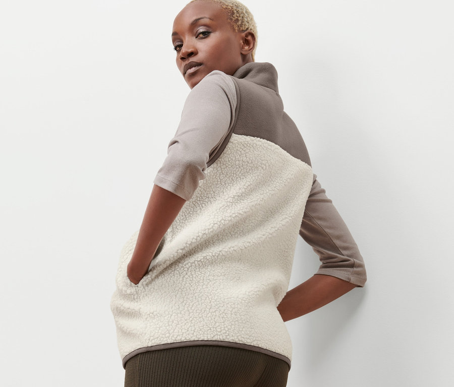 Nő pózol egy bézs-barna plüss mellényben.