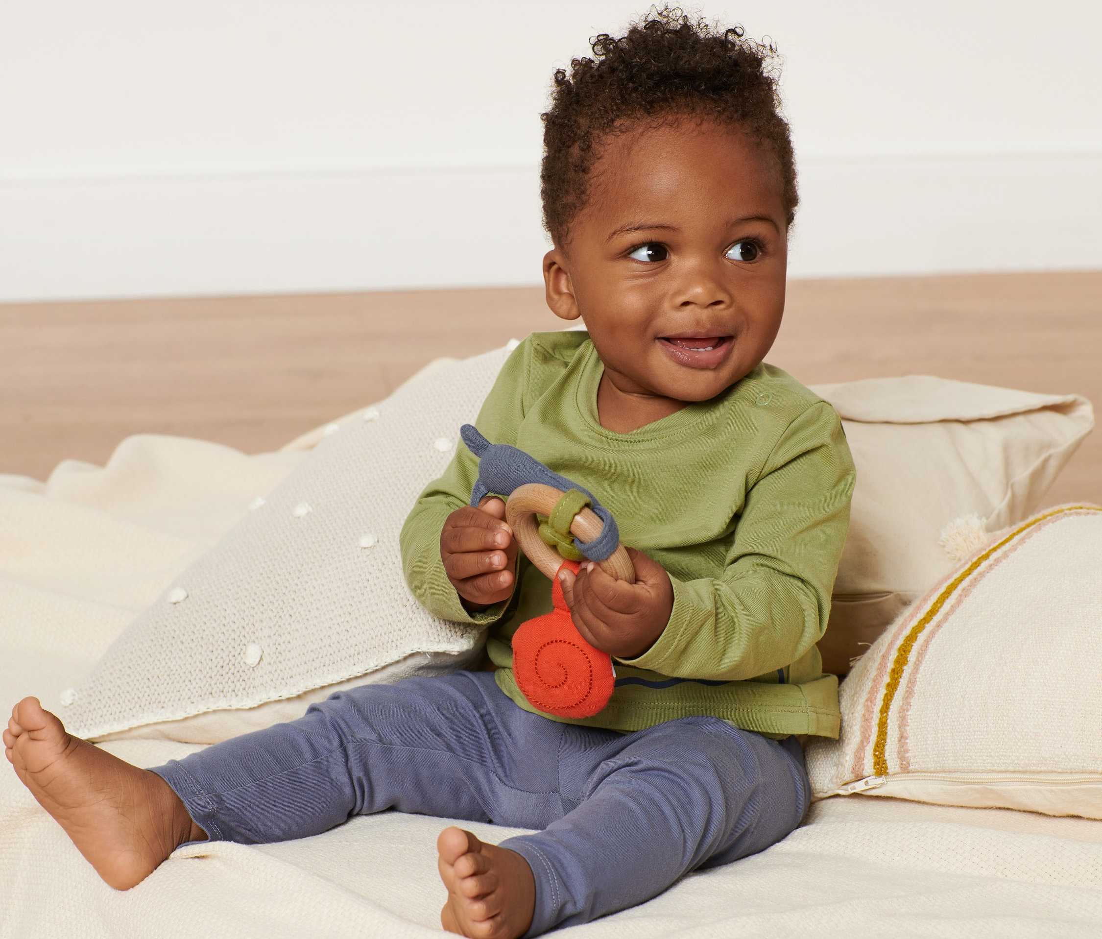 Mosolygó baba ül egy takarón és egy csörgőt tart.