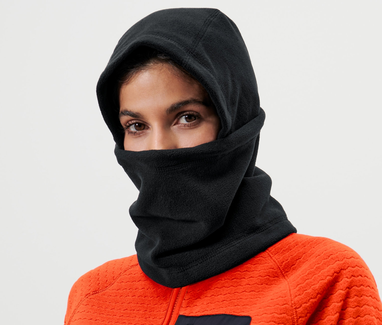 Nő visel fekete mikropolár kámzsát és narancssárga kabátot.