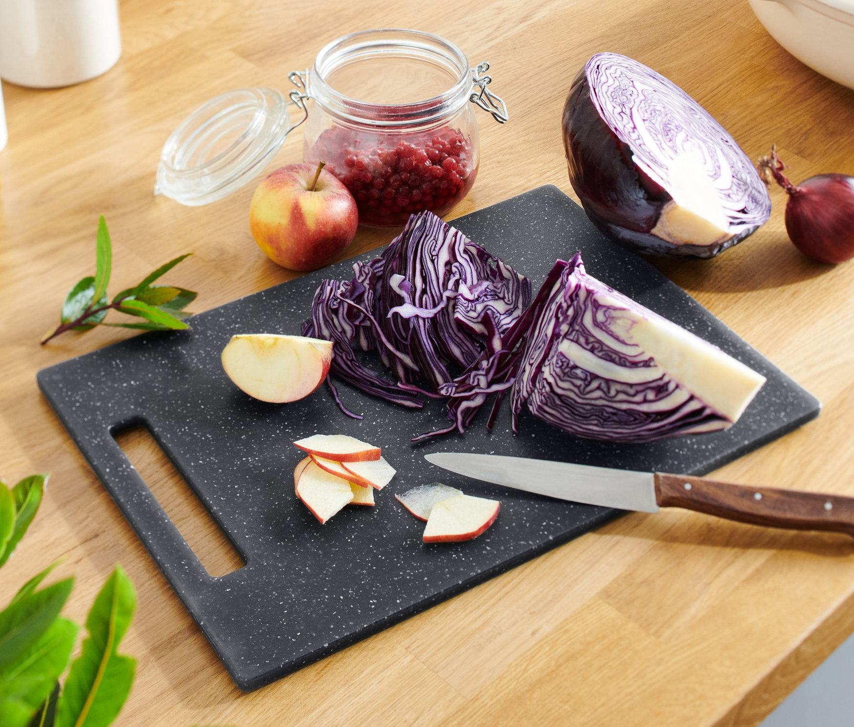 Vágott vörös káposzta és alma egy gránithatású vágódeszkán késsel.