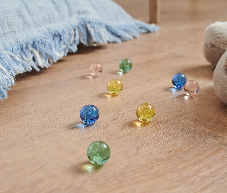 Színes üveggolyók vannak a padlón egy plüsskutya és egy kék takaró mellett.