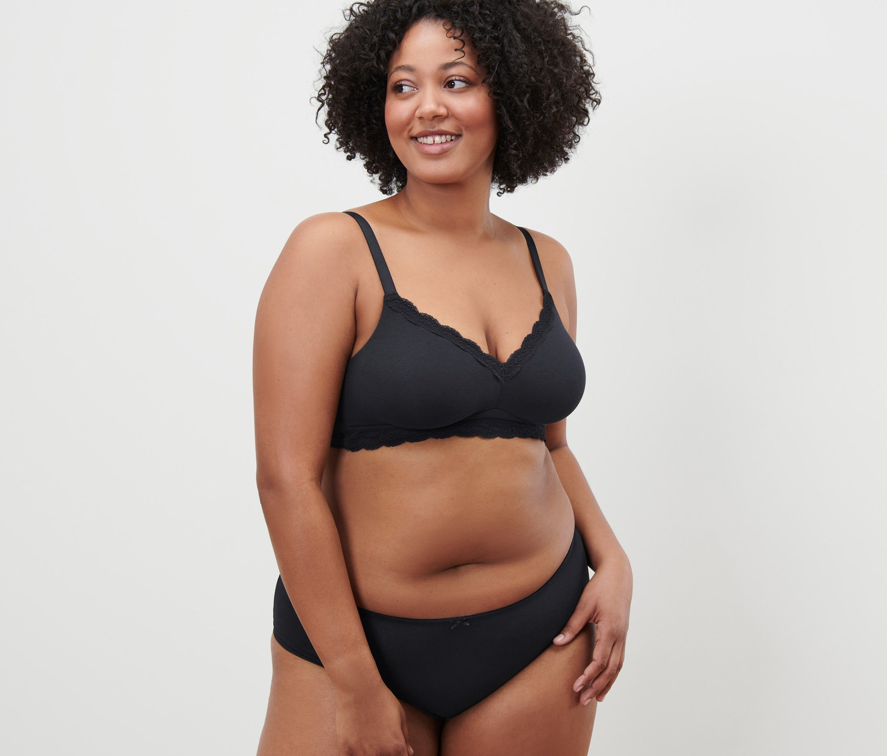 Göndör hajú nő pózol fekete, puha melltartóban.