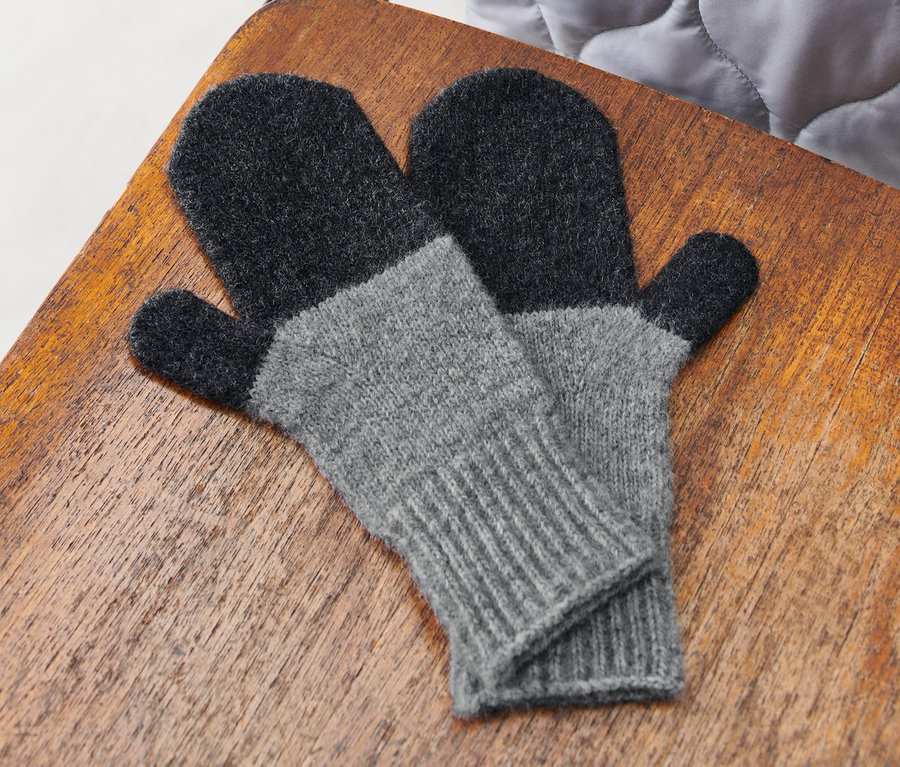 Egy pár világosszürke kötött egyujjas kesztyű fekszik egy fa széken.