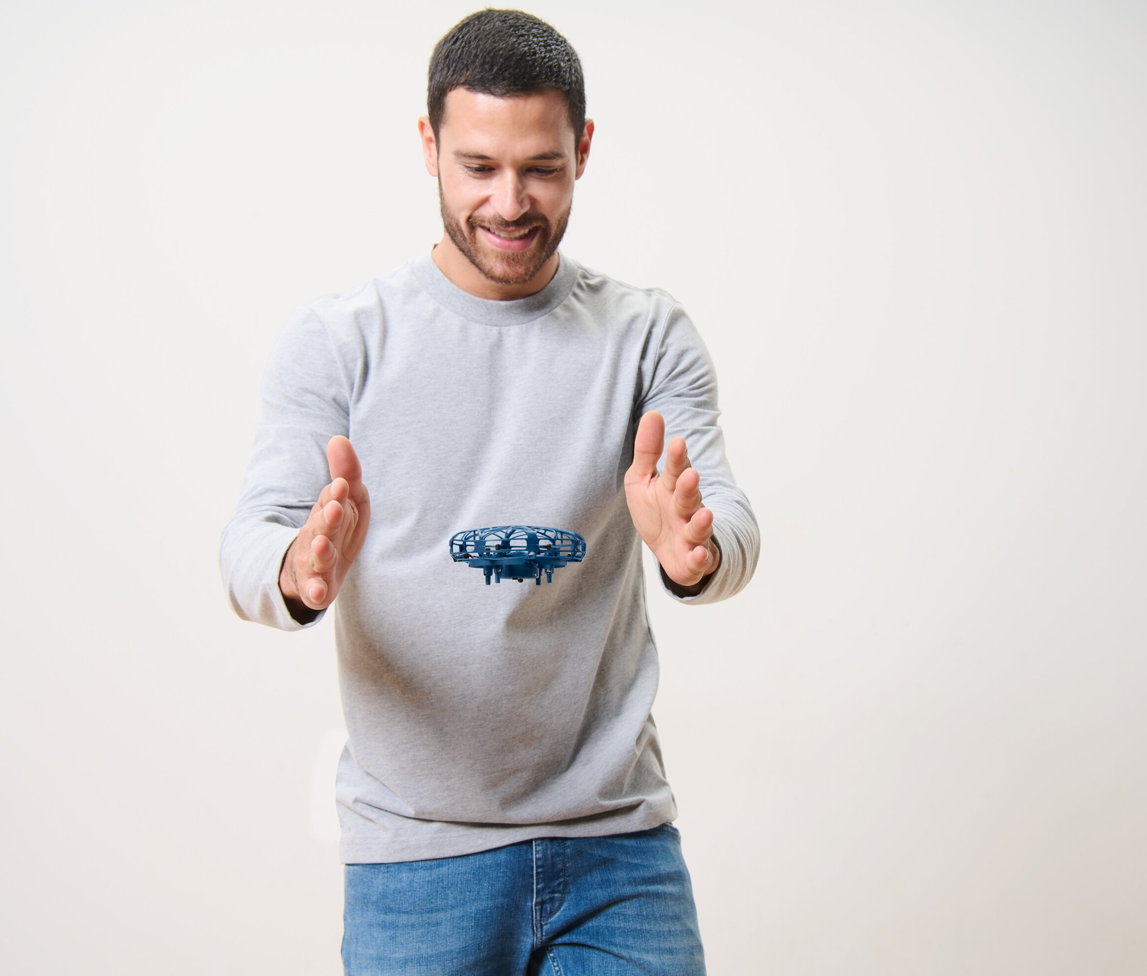 Egy férfi mosolyog, és a kezei között repülő mini drónt nézi.