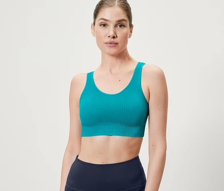 Nő visel egy türkiz varrásmentes bustier sportmelltartót.