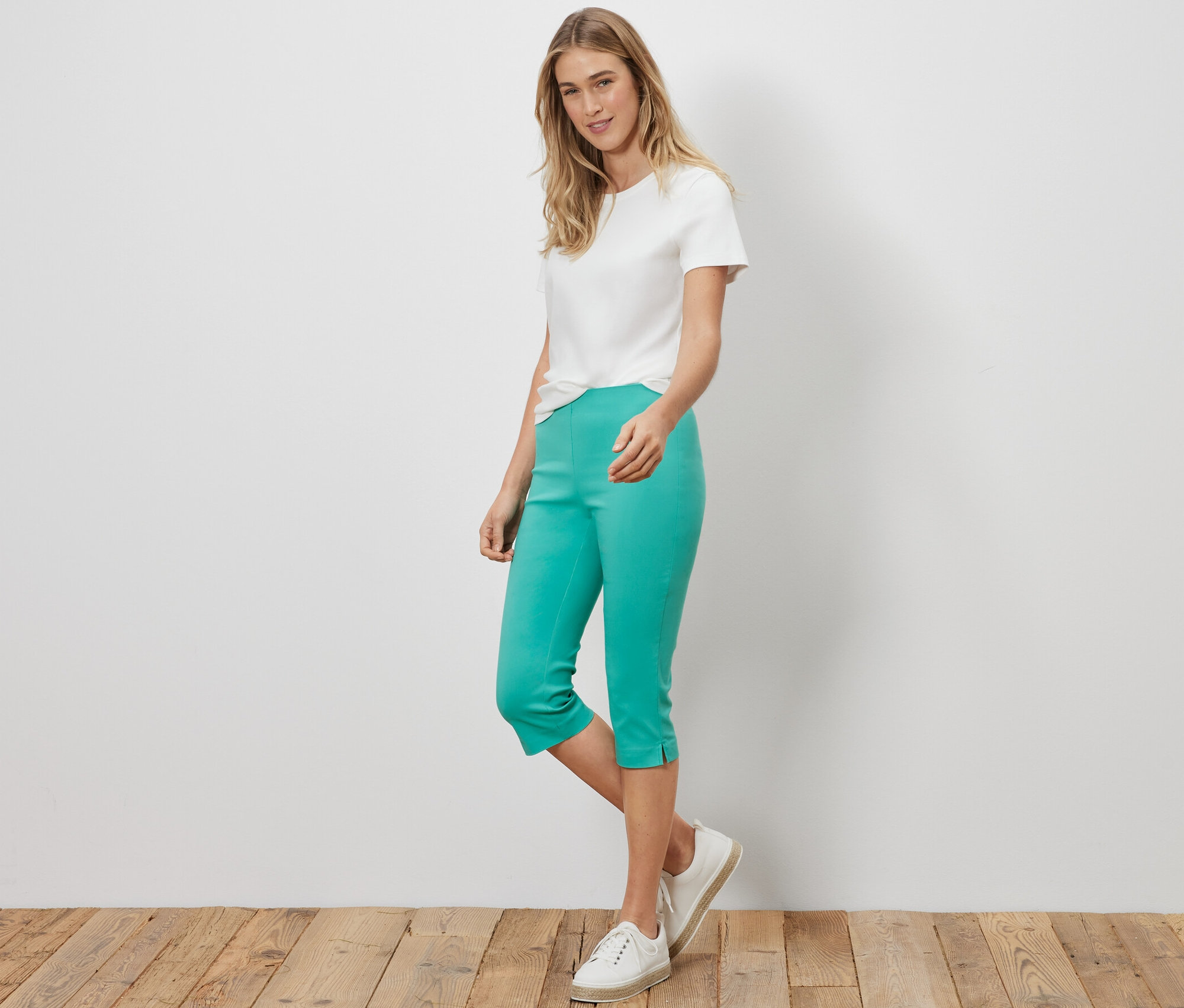 Nő áll fehér pólóban és türkiz 3/4-es sztreccsnadrágban.
