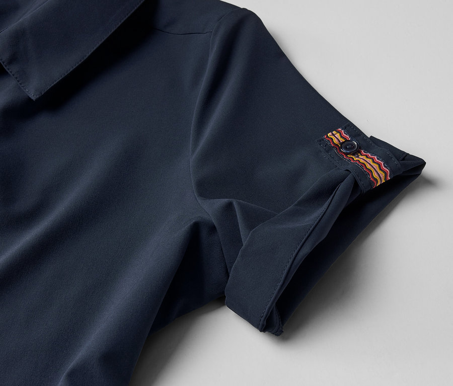 A sötétkék női funkcionális ruha részlete, gombbal az ujján.