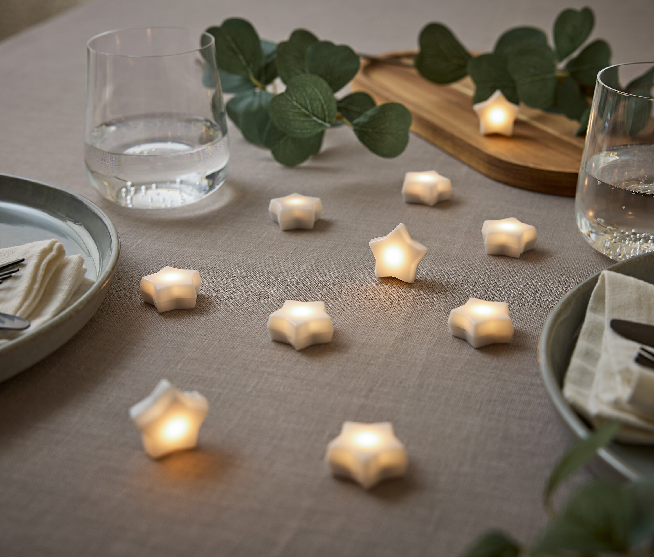 Megterített asztal csillagokkal, tányérokkal, vizespoharakkal és eukaliptusszal.