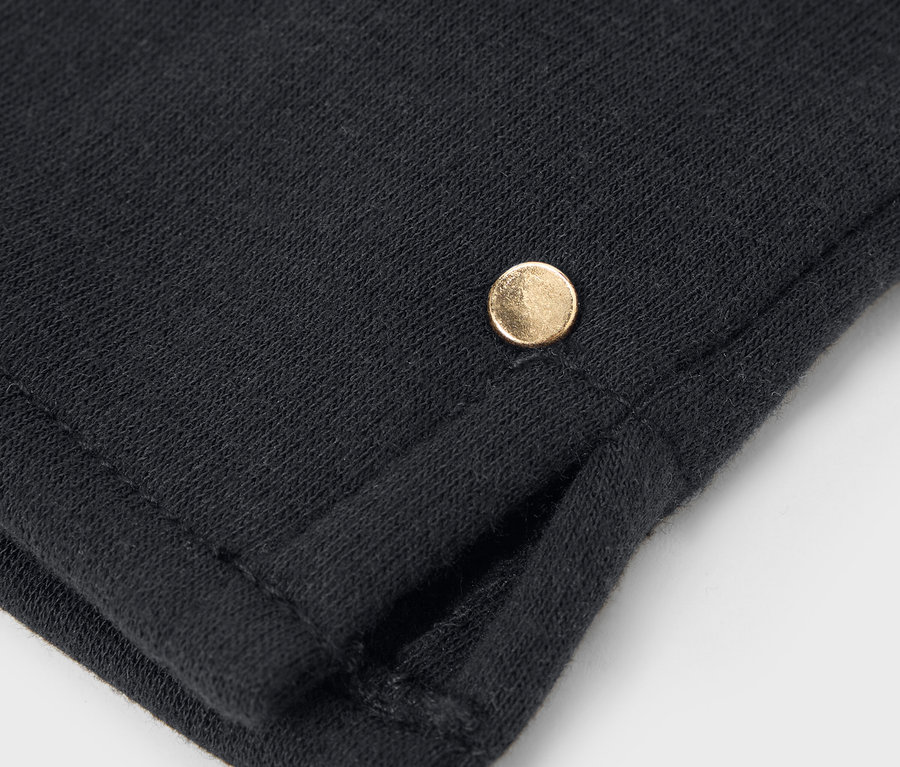 Közelkép egy fekete anyagról, rajta egy kis arany gombbal.