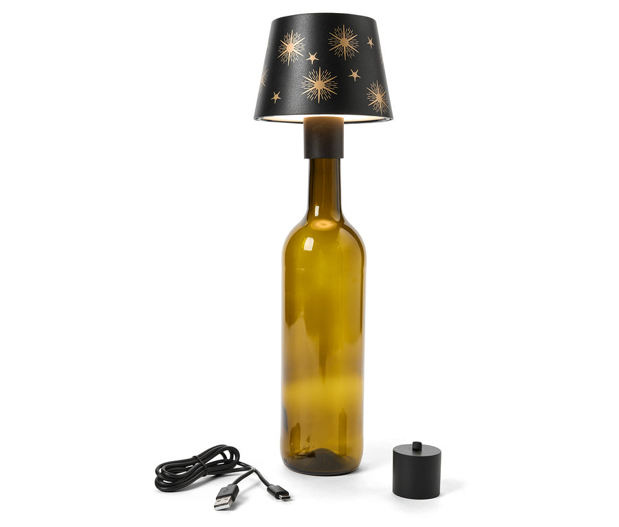 Olívazöld üvegpalackból készült asztali lámpa fekete, arany csillagokkal díszített lámpabúrával. Egy USB-kábel és egy fekete kapcsoló a lámpa mellett fekszik.