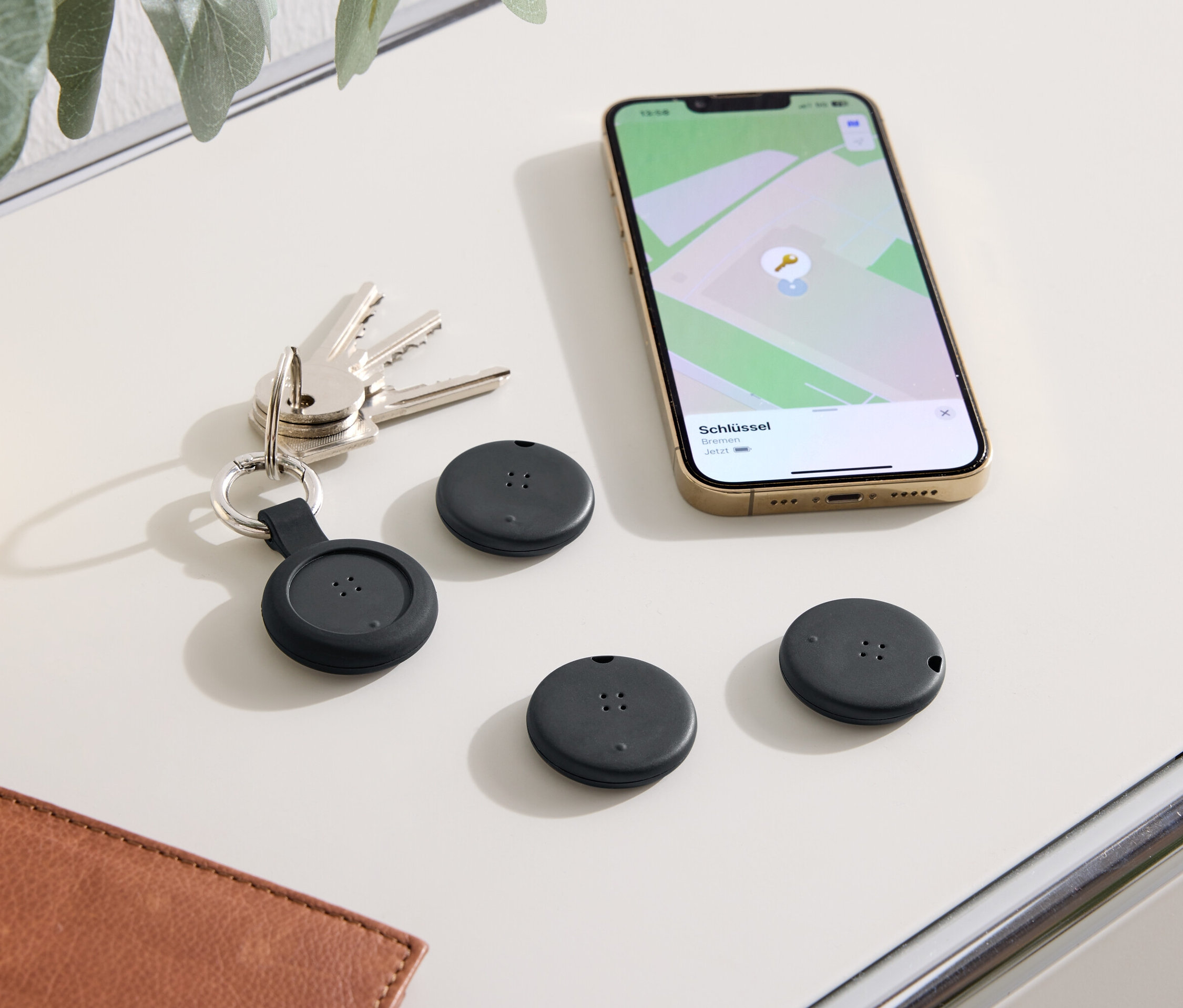 Az asztalon kulcsok, egy telefon térképpel és három fekete helymeghatározó eszköz található.