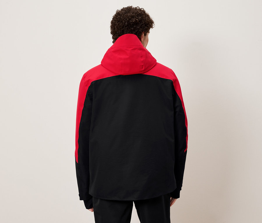 Egy férfi háttal a kamerának fekete és piros kapucnis kabátot visel.