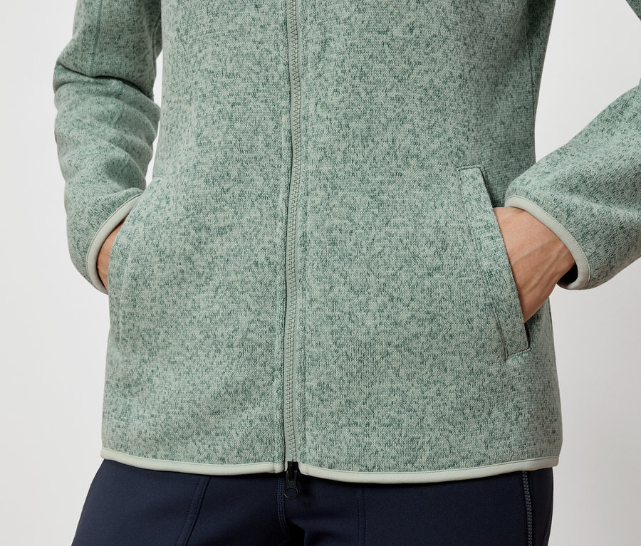 Egy személy a zöld polárkabát zsebében tartja a kezét.