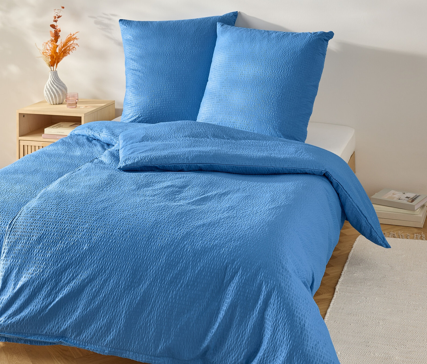 Kék krepp ágynemű normál méretben egy ágyon éjjeliszekrénnyel.