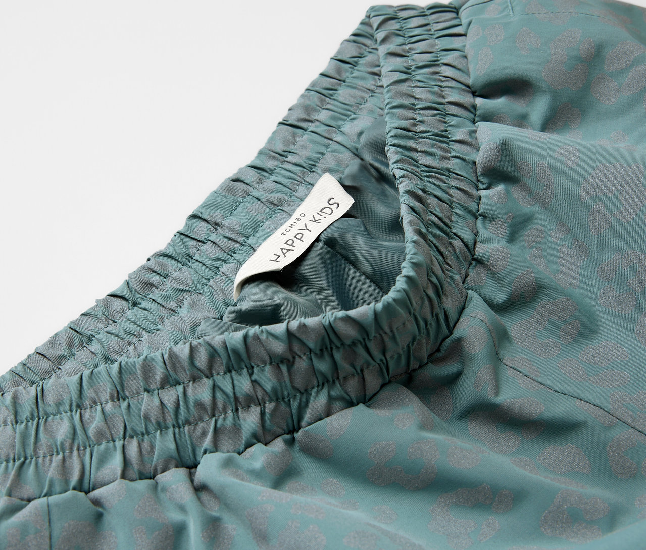 Közeli kép egy fényvisszaverő elemekkel ellátott gyerek esőnadrágról, rugalmas derékpánttal és Happy Kids címkével.