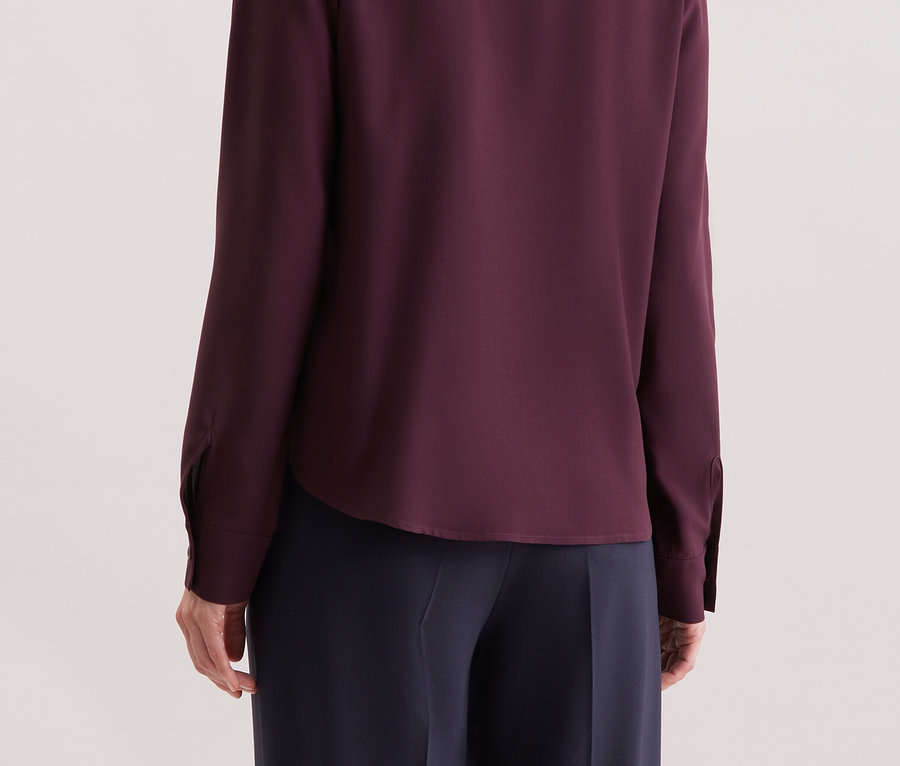 Hátulról látható egy szőke hajú nő, aki egy lila, hosszú ujjú inget visel.